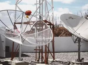 Com a implementação do 5G, as parabólicas tradicionais, que operam na faixa de 3,5 GHz, serão desativadas, levando à necessidade de substituição por parabólicas digitais. Mais de 1,6 milhão de famílias de baixa renda em todo o Brasil, incluídas no Cadastro Único para Programas Sociais do Governo Federal (CadÚnico), já foram beneficiadas com a substituição de seus equipamentos antigos por kits contendo a nova parabólica digital, em 2023. O ministro das Comunicações Juscelino Filho reitera a importância de fazer essa substituição: “A troca pela parabólica digital garante mais qualidade de som e imagem e permite que as famílias continuem desfrutando da programação variada com ainda mais qualidade". A tecnologia 5G opera na mesma faixa da radiofrequência das parabólicas tradicionais, conhecida como Banda C. Isso significa que quem utiliza parabólicas tradicionais para assistir TV precisará adotar novos equipamentos, incluindo a parabólica digital e um receptor compatível com a Banda Ku. A migração da Banda C para a Banda Ku proporciona uma limpeza na faixa de 3,5 GHz, resultando em uma melhoria significativa na qualidade de som e imagem da TV. COMO SOLICITAR A NOVA PARABÓLICA DIGITAL? A ação de substituição está disponível para cidades com mais de 500 mil habitantes, e a solicitação do kit gratuito pode ser feita através do portal Siga Antenado ou pelo telefone 0800 729 2404. O kit inclui parabólica digital, receptor, controle remoto com pilhas e cabos necessários. O agendamento e instalação são realizados por técnicos do Siga Antenado, garantindo uma transição tranquila para a nova tecnologia. O agendamento e a instalação dos kits gratuitos com a nova parabólica digital estão disponíveis para mais 3.283 municípios. De acordo com a Anatel, essa liberação da faixa não significa que redes do 5G serão instaladas de imediato nas localidades. A instalação antecipada de estações de quinta geração depende do planejamento individual de cada prestadora.